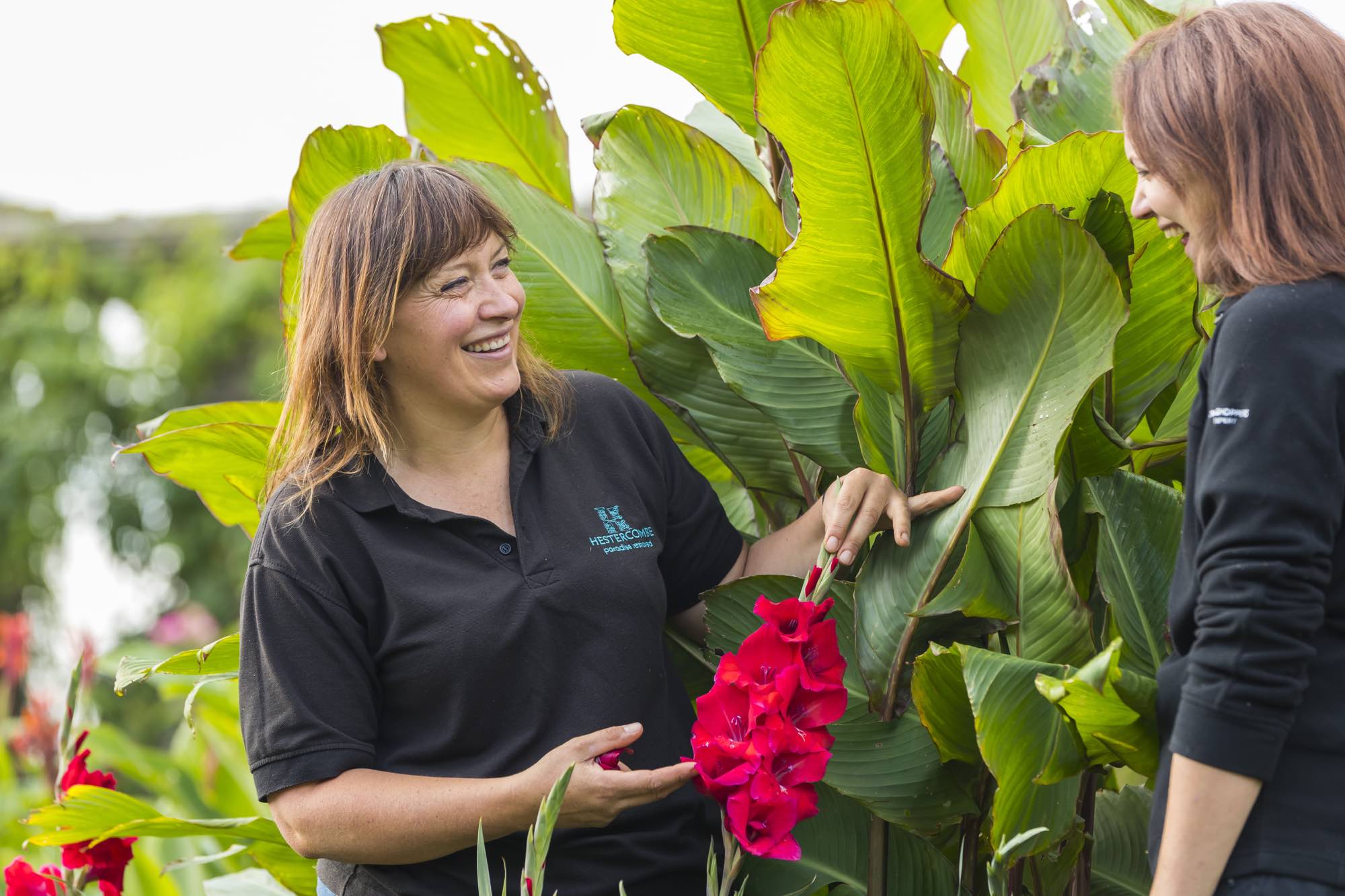 Claire Greenslade next to a red flowering plant in the garden at Hestercombe