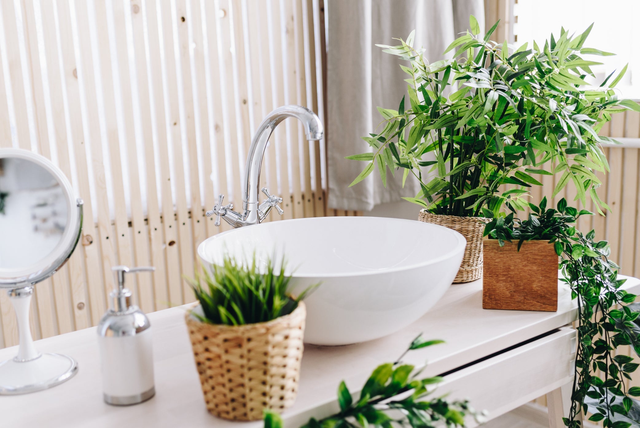 various potted houseplants decorated around a white sink in a bathroom in front of a panelled wall and window