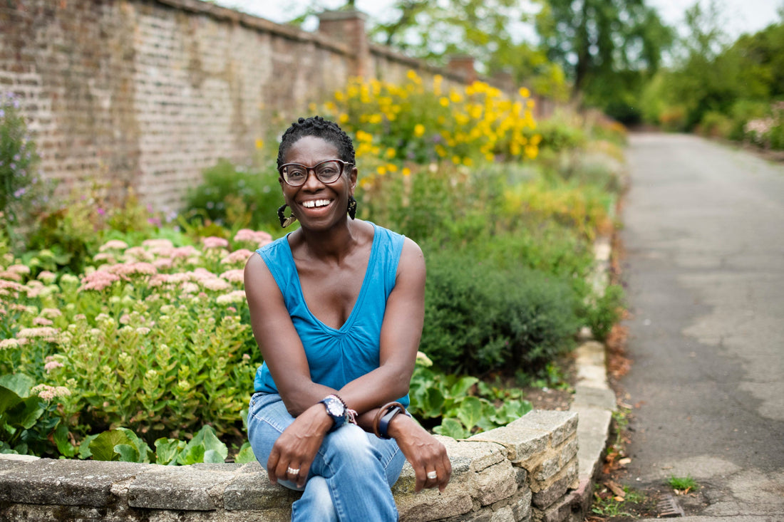 Flo Headlam sitting on a wall of a garden filled with colourful shrubs and plants