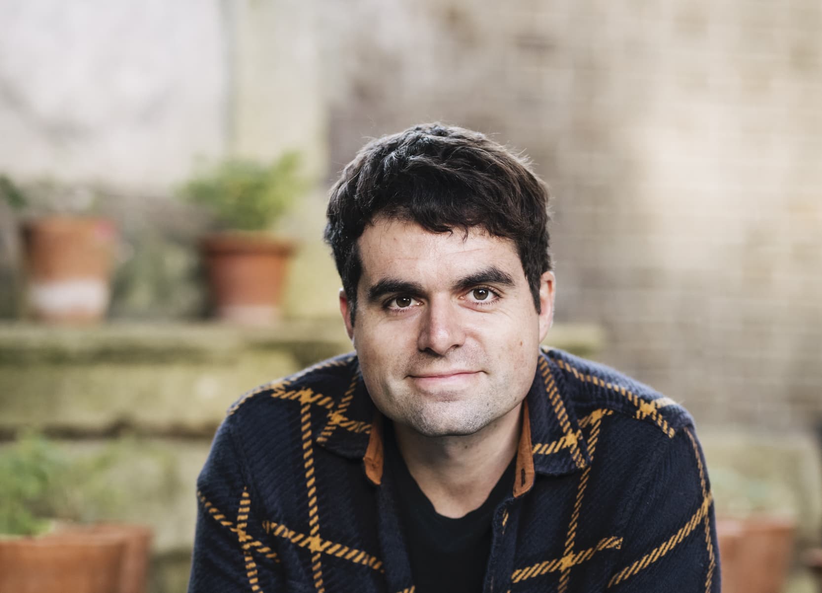 Matt Collins in the garden with small potted plants on a wall behind him