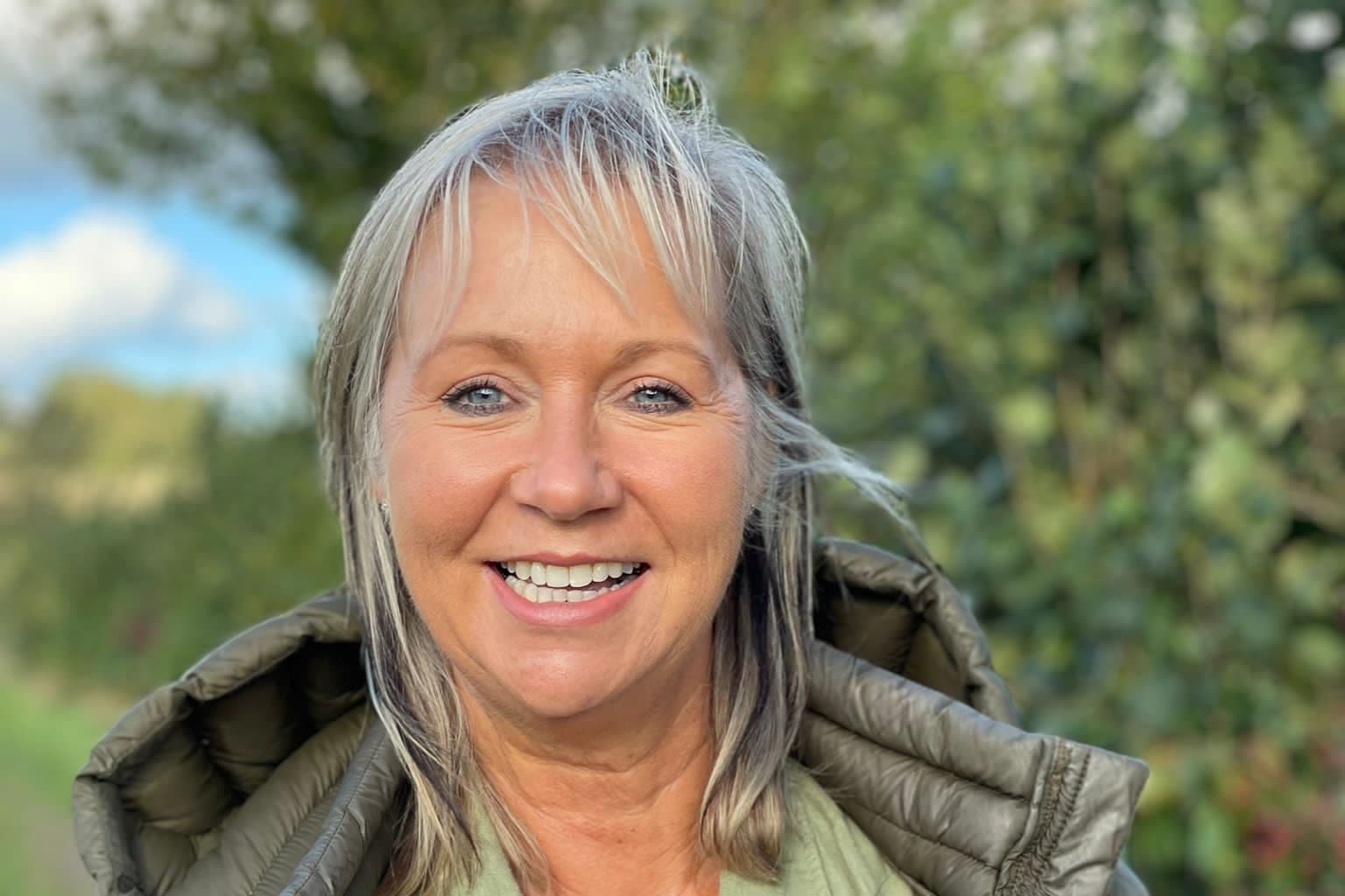 Raine Clarke-Willis headshot taken outside in a garden on a sunny day