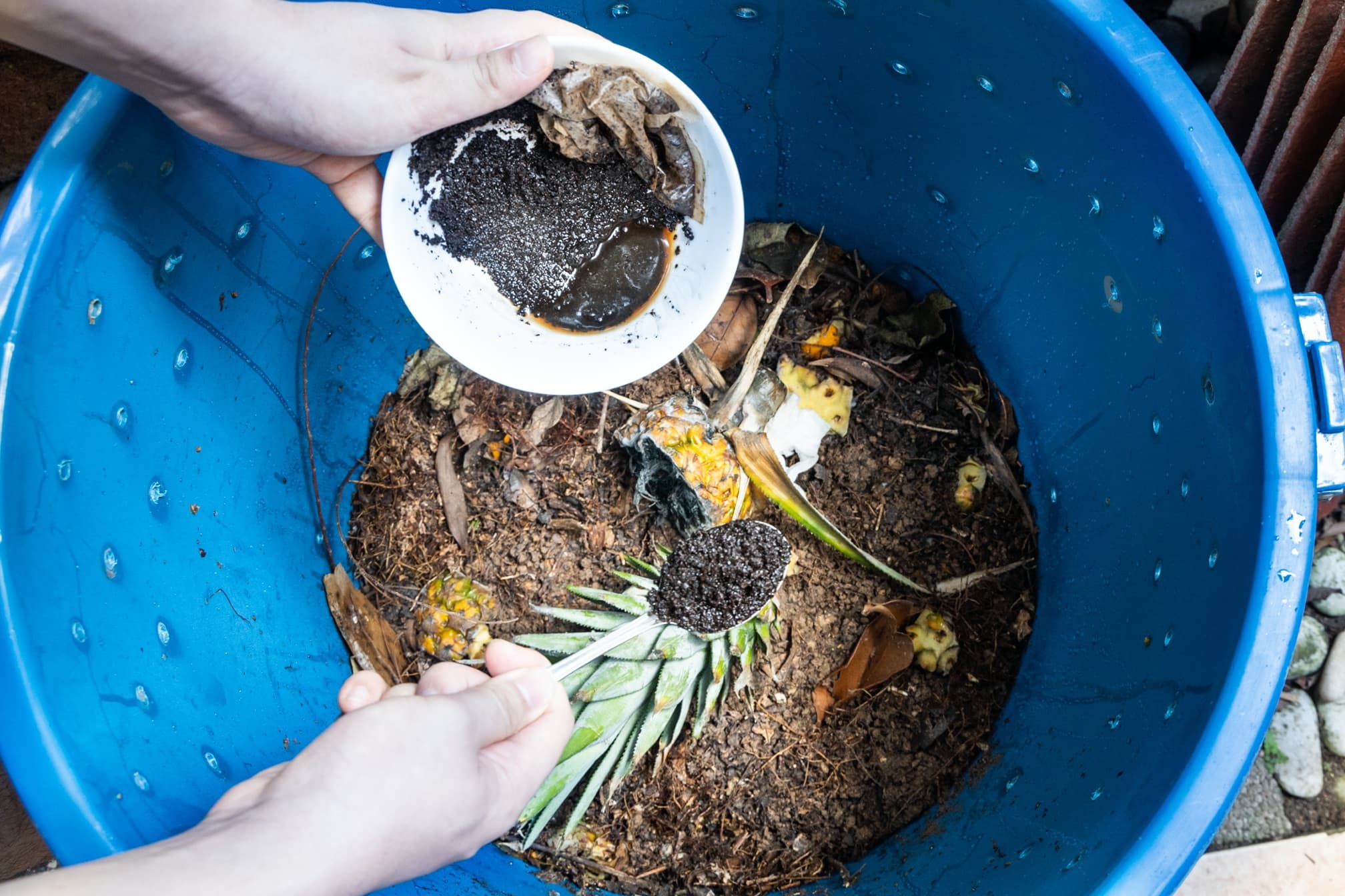 hand adding grounds to a compost bin