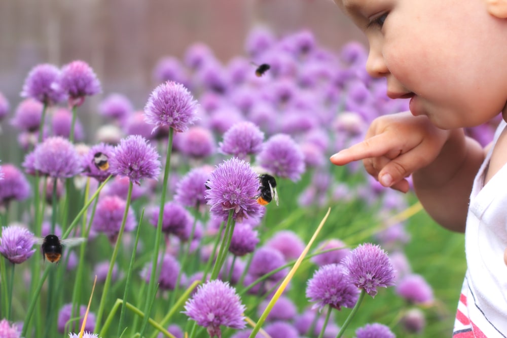 A small child points a finger at a bumblebee on a flower