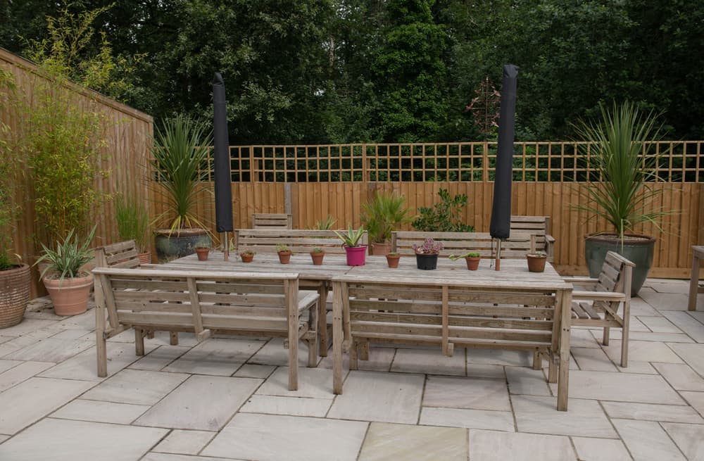 paved patio with surrounding timber fences, plants in pots and wooden furniture