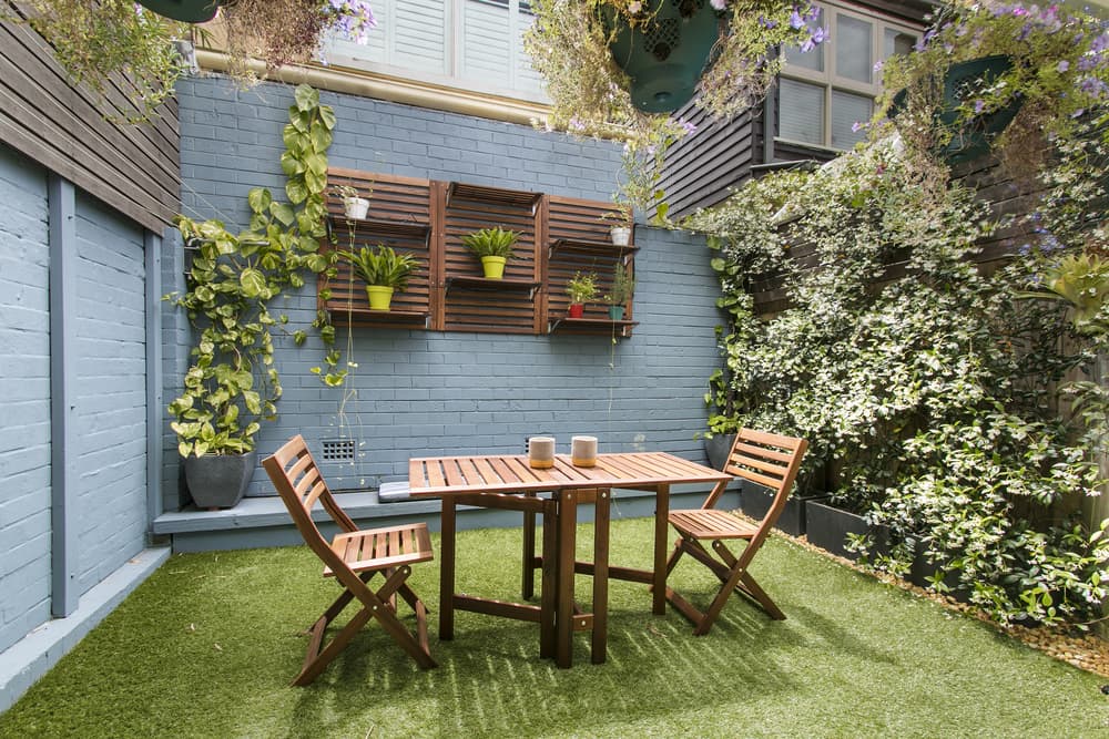 a small outdoor area with artificial grass, potted plants and high walls and screens for privacy