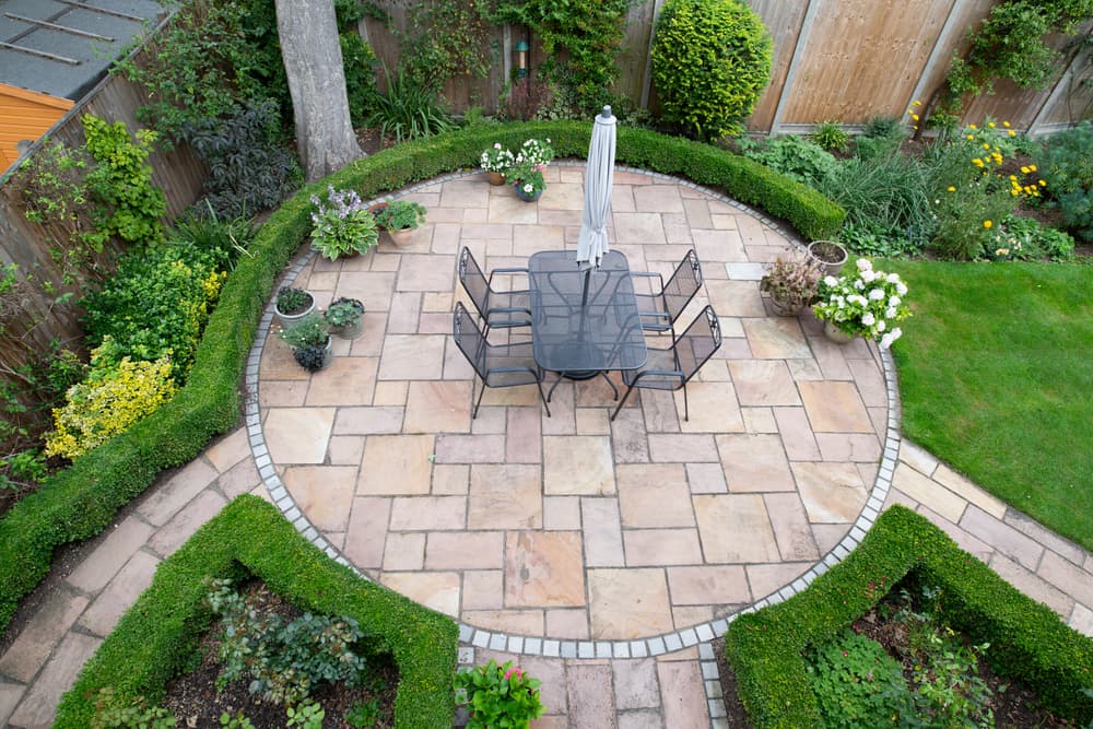 birds eye view of a large circular patio space, with garden furniture sat in the middle and hedging and plants growing around the outside