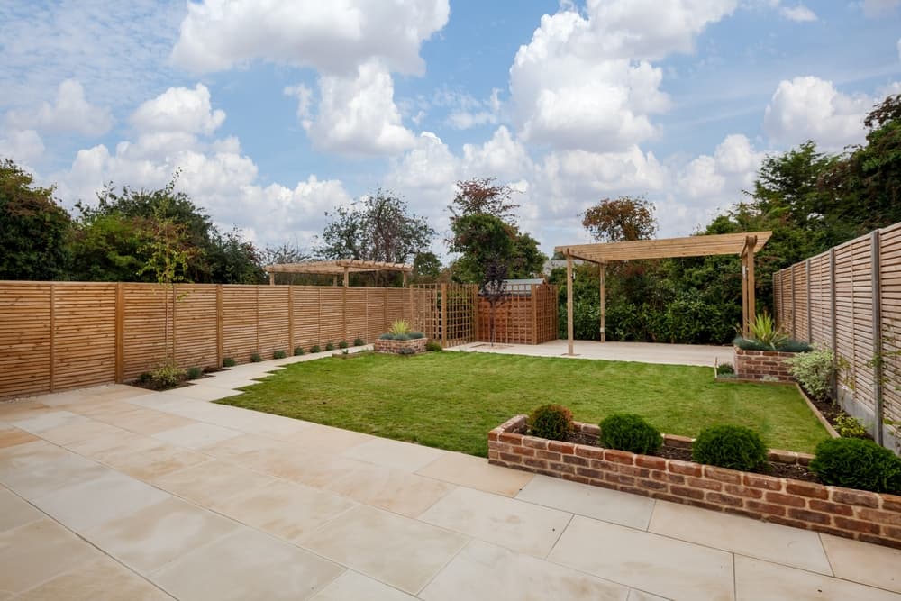 a freshly landscaped garden with extensive paved area, a lawn, shed and pergola