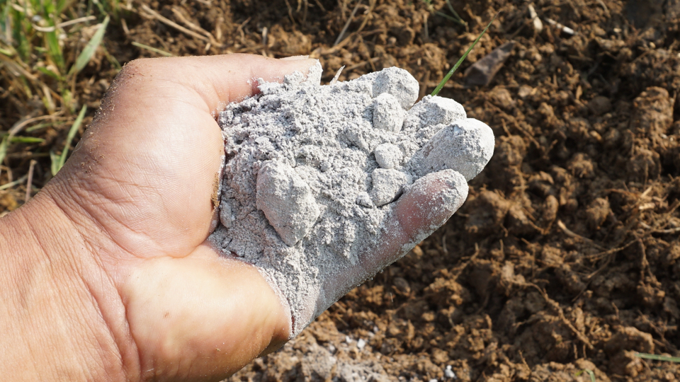 a hand holding a handful of ashes over some soil