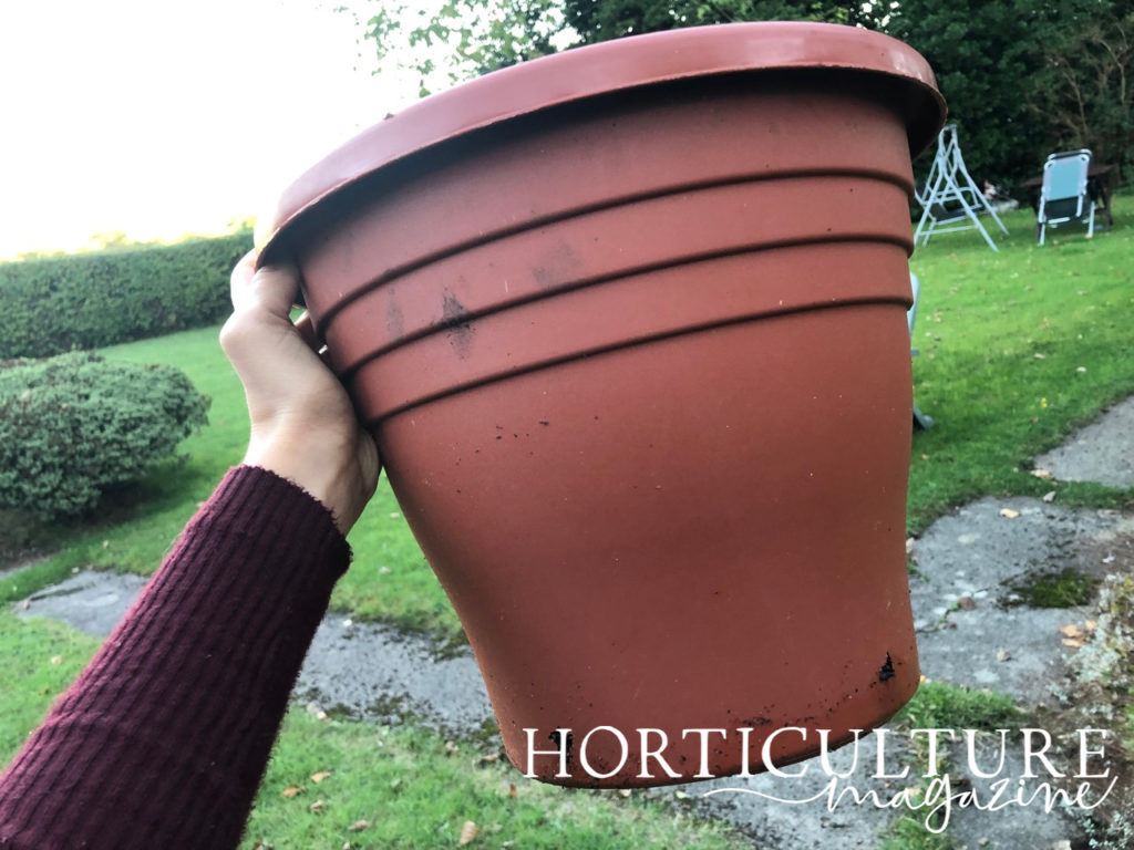 a large brown pot being held up in front of a garden outside
