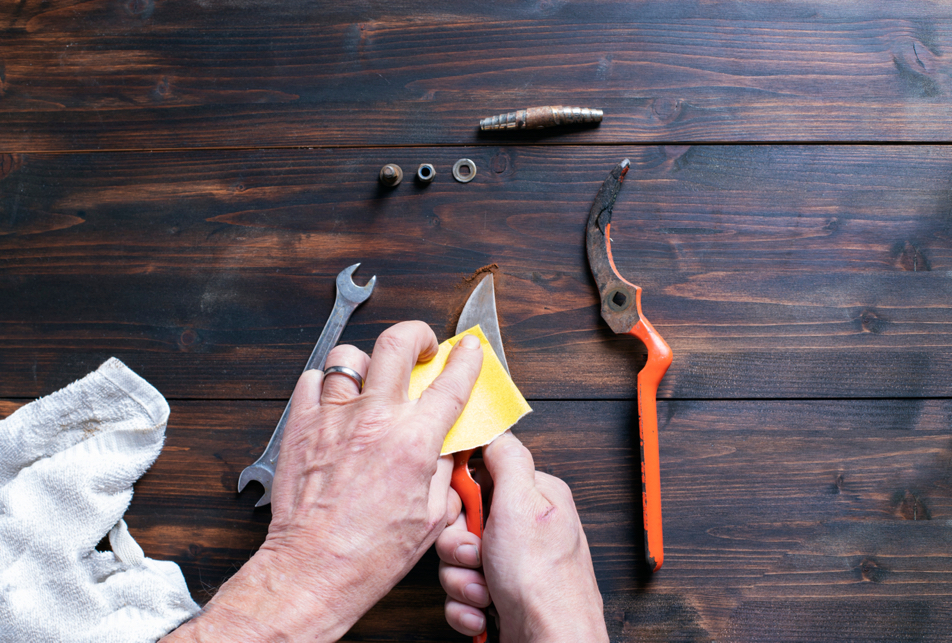 gardening secateurs being wiped down with a yellow cloth on a wooden surface