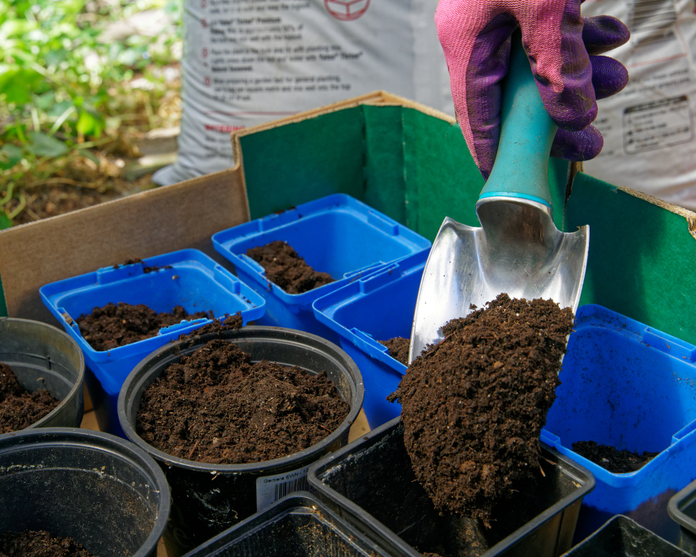 someone using a spade to fill various small pots with compost mix 