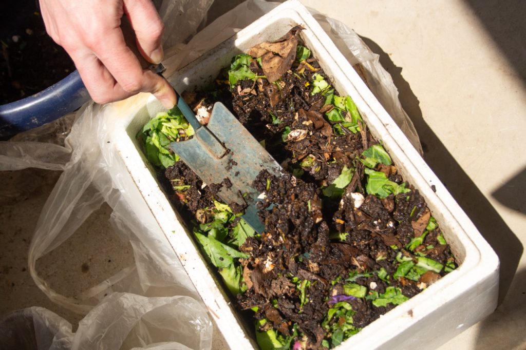 homemade compost bin with a brown and green mix being dug into my a gardening trowel