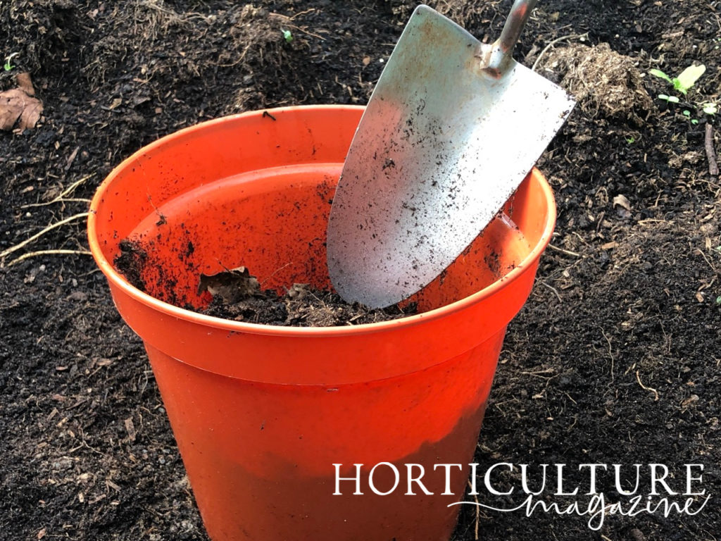 a trowel being used to scoop up compost in a small orange container