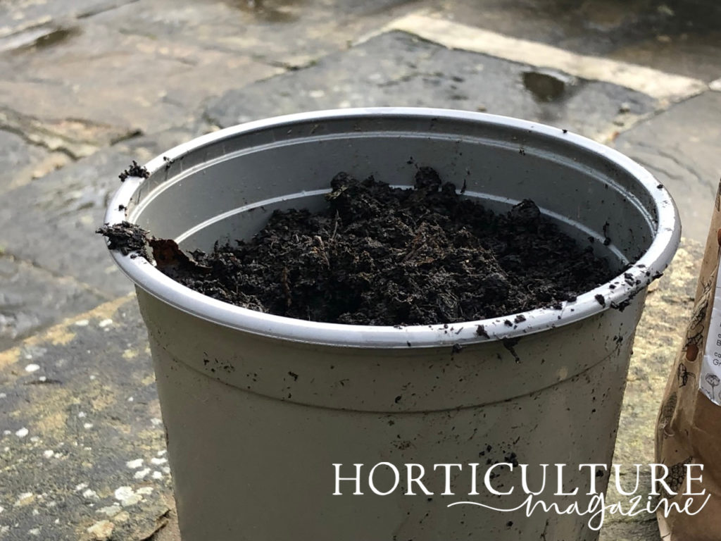 a large grey container full of compost placed outside on a stony patio floor