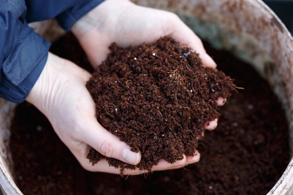 hands holding a handful of compost over a huge container