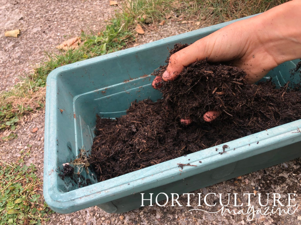 gardener adding compost by hand into a large container outside