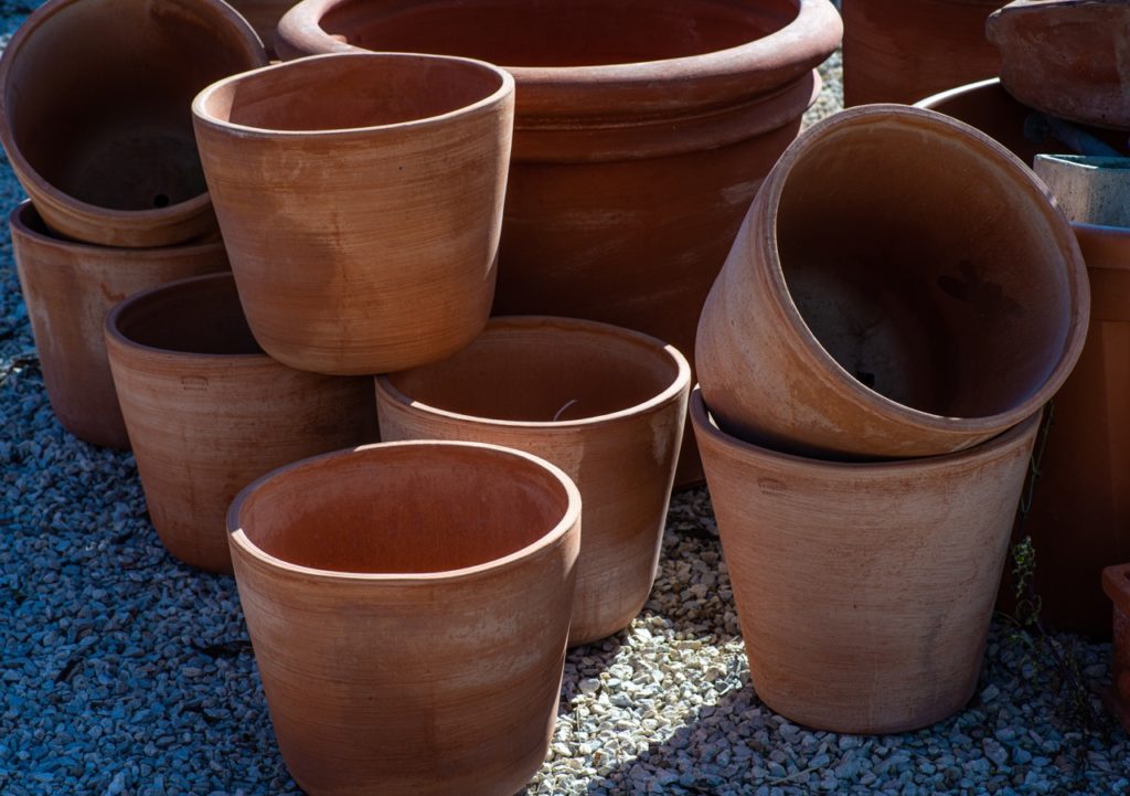 lots of brown terracotta plant pots on some gravel, with some stacked on top of one another