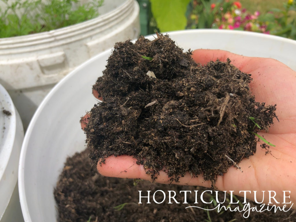 someone holding a handful of compost in front of a container full