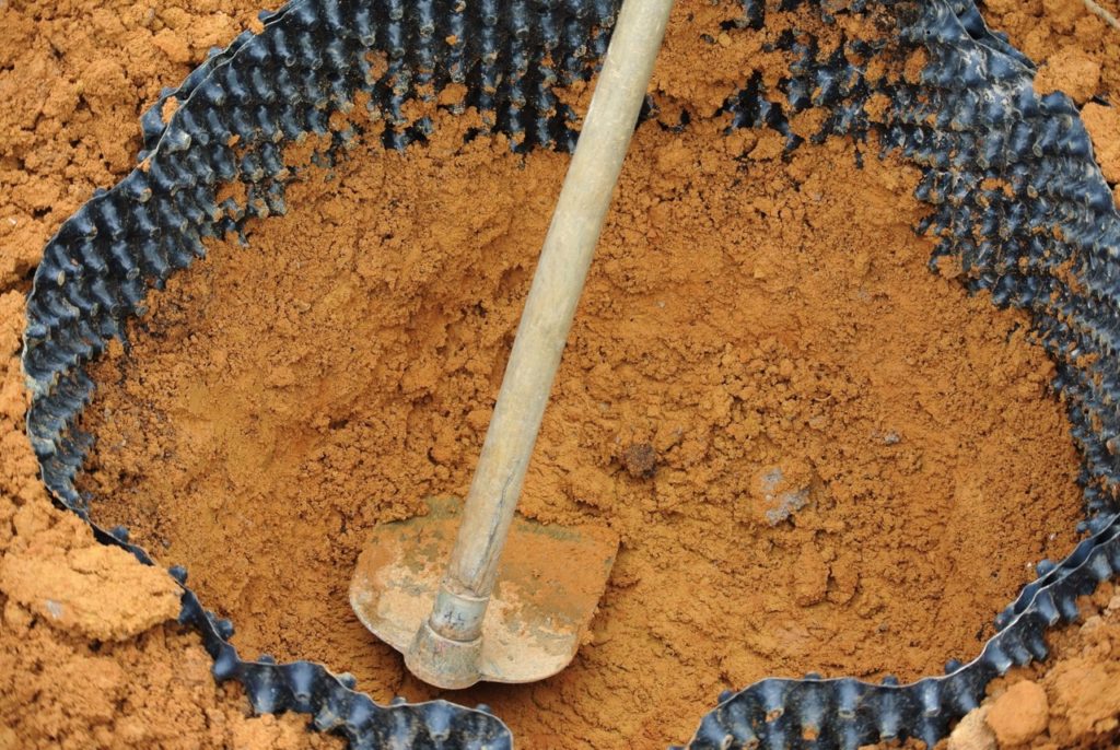 clay soil that is bordered by a plastic root barrier being dug up by a garden hoe