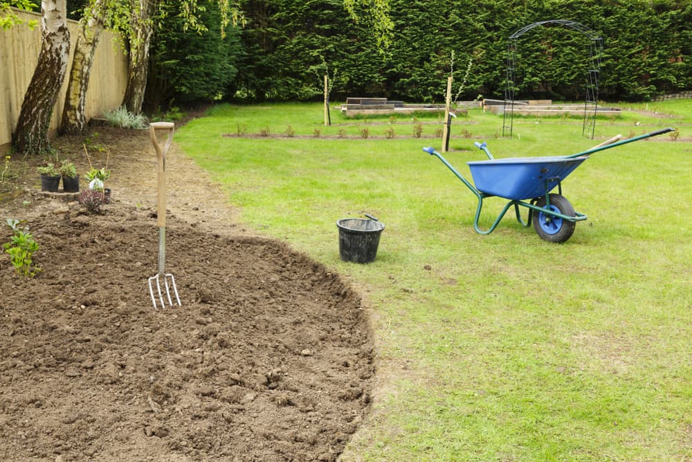 an empty garden border ready for planting with a wheelbarrow and garden fork