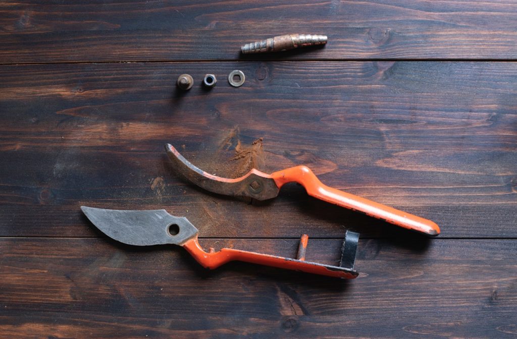 a dismantled pair of secateurs with an orange handle lying on a wooden table