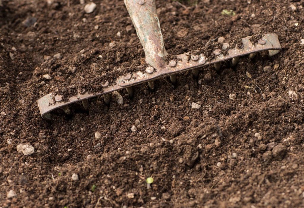 a metal rake being used to till soil with lots of stones mixed into it