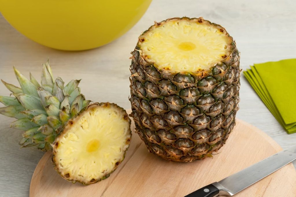 the top of a pineapple and its main body next to a knife and chopping board
