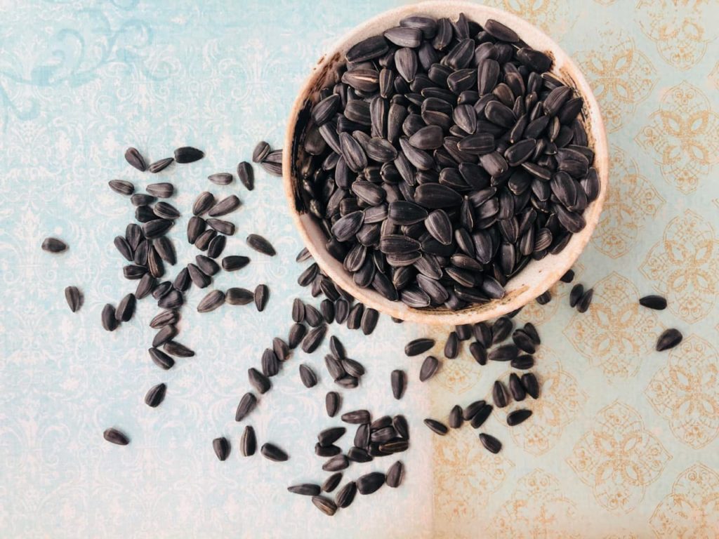 a bowl full of black sunflower seeds that are also scattered onto the table
