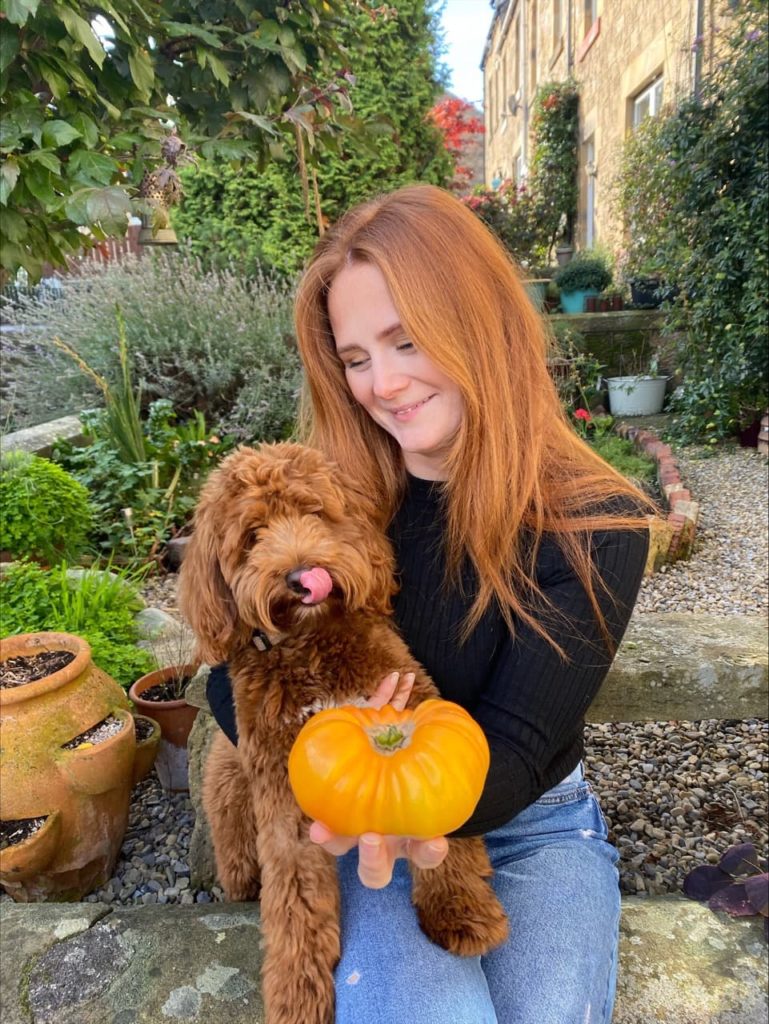 Hannah Reid 'Ginger Grows' and her dog posing with a small pumpkin in her garden