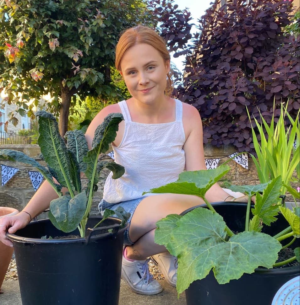 Hannah Reid with some large green leafy plants like kale and courgettes growing in black pots