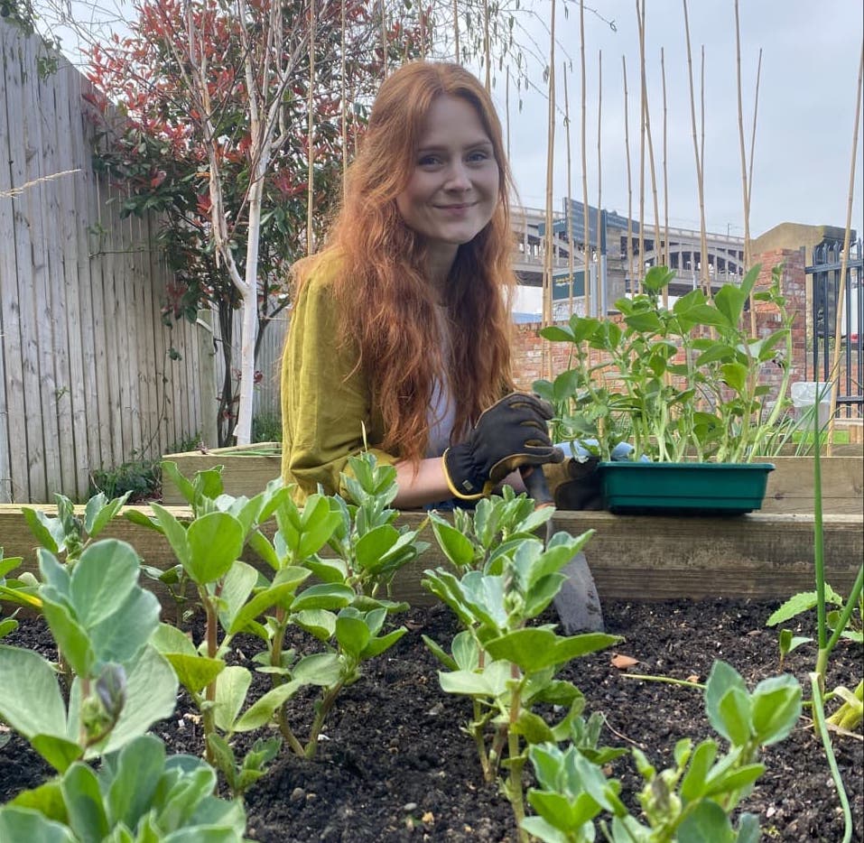 Hannah smiling behind her raised beds as she plants out seedlings