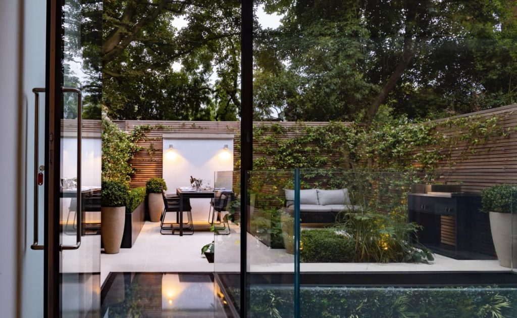 modern garden with a water feature and climbing green plants covering the surrounding wall designed by Kate Gould
