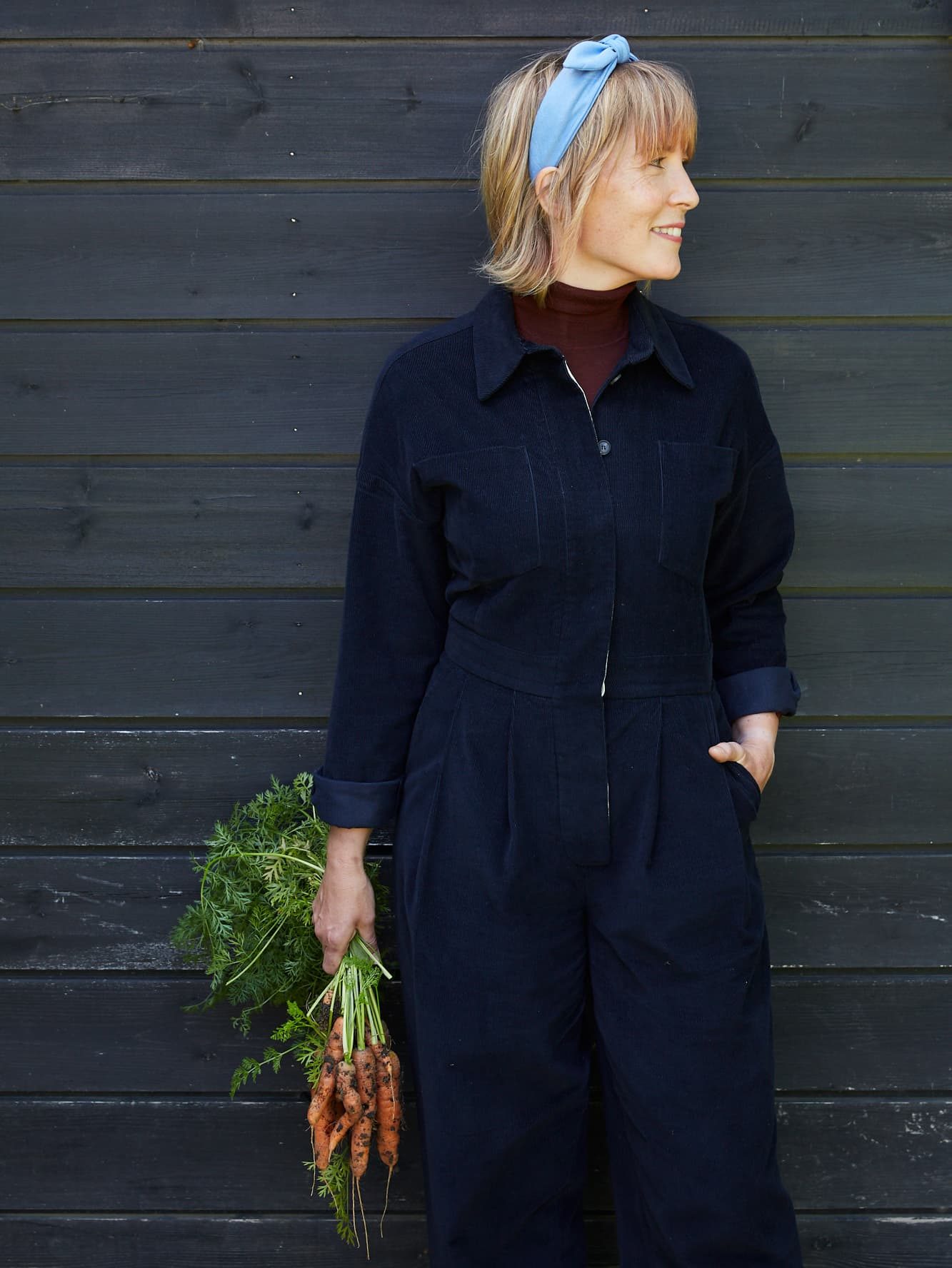 Kathy slack holding harvested carrots in front of a wooden shed