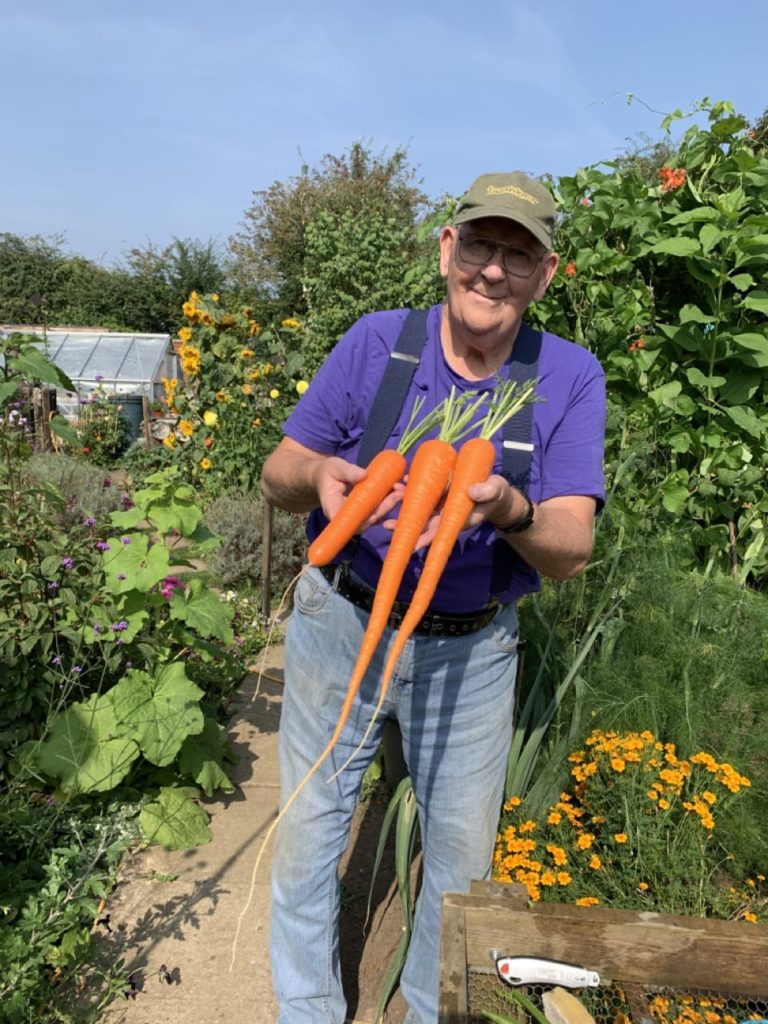 gerald holding up some large carrots he has just harvested from his garden