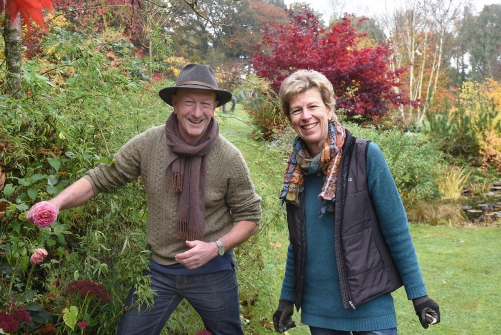 Andy Mcindoe and his wife Ros in their garden next to a pink flowering rose shrub