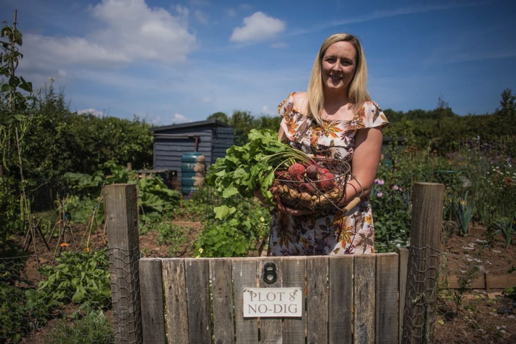 Jenny Thompson on her allotment holding a basket of harvested radishes and potatoes