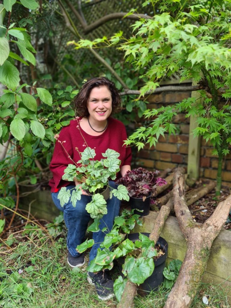 Naomi Slade crouching in a garden holding some potted heuchera plants