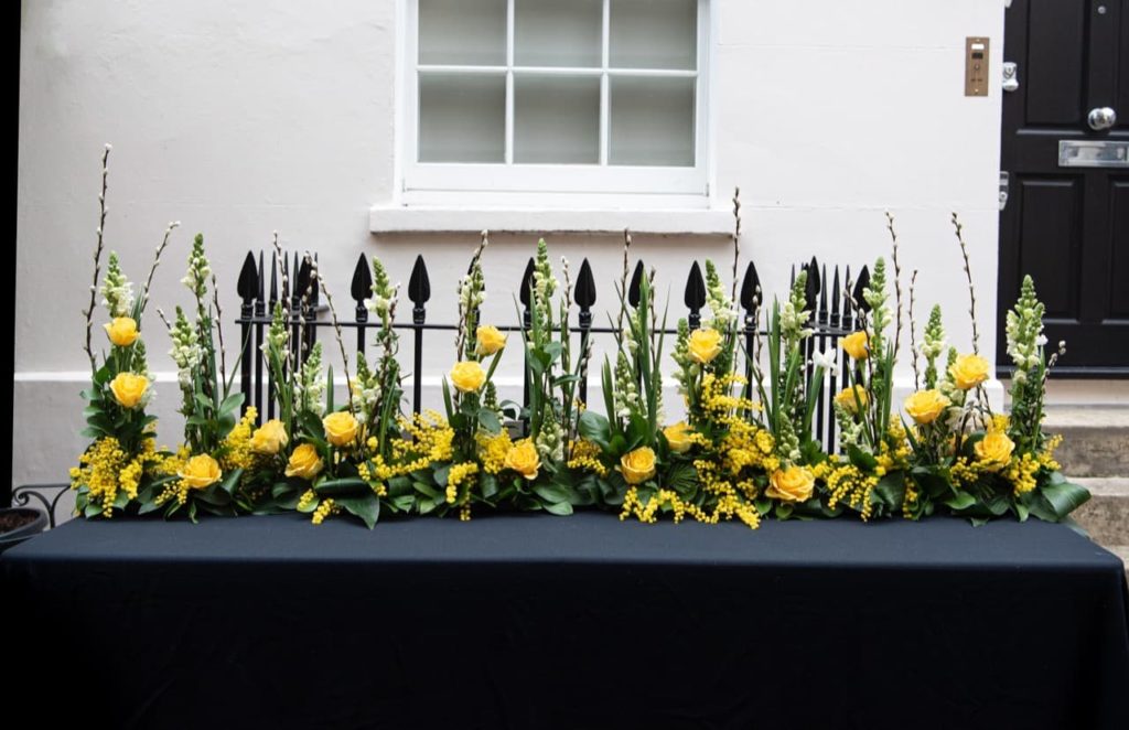 yellow roses and other flowers in a floral design by Judith Blacklock growing along a table outdoors