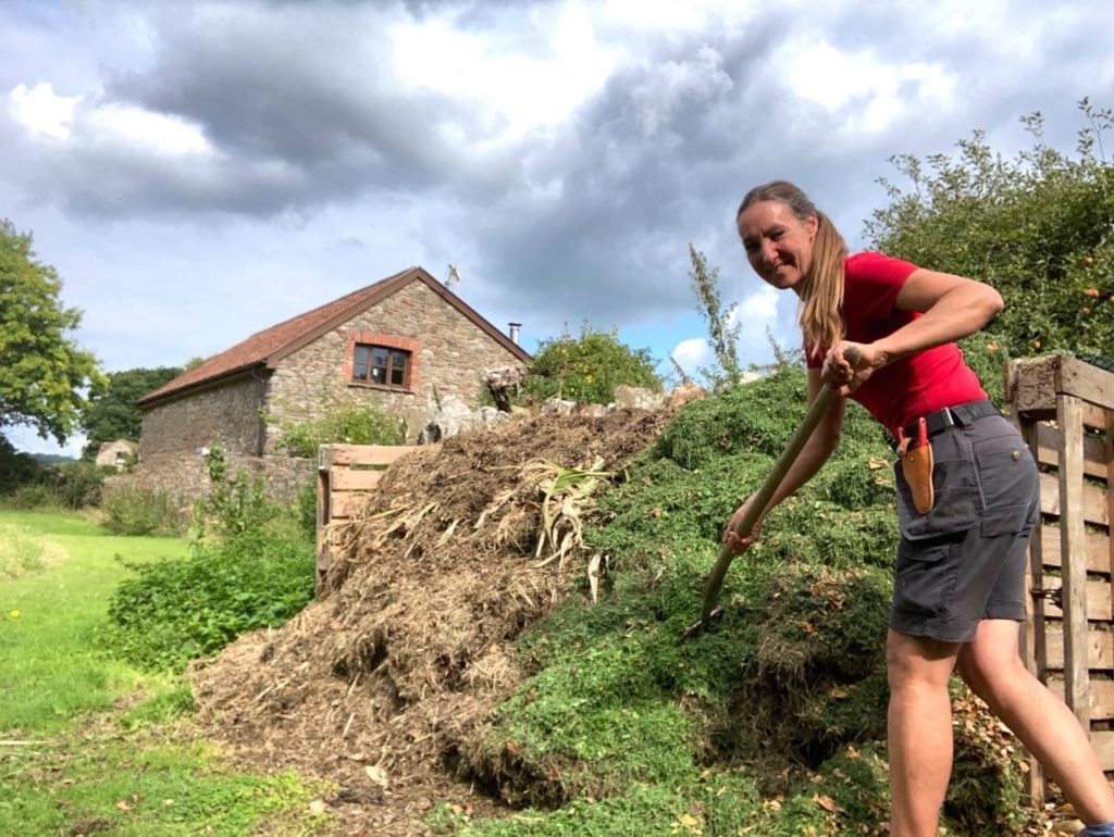 Debi digging into a compost heap full of grass clippings