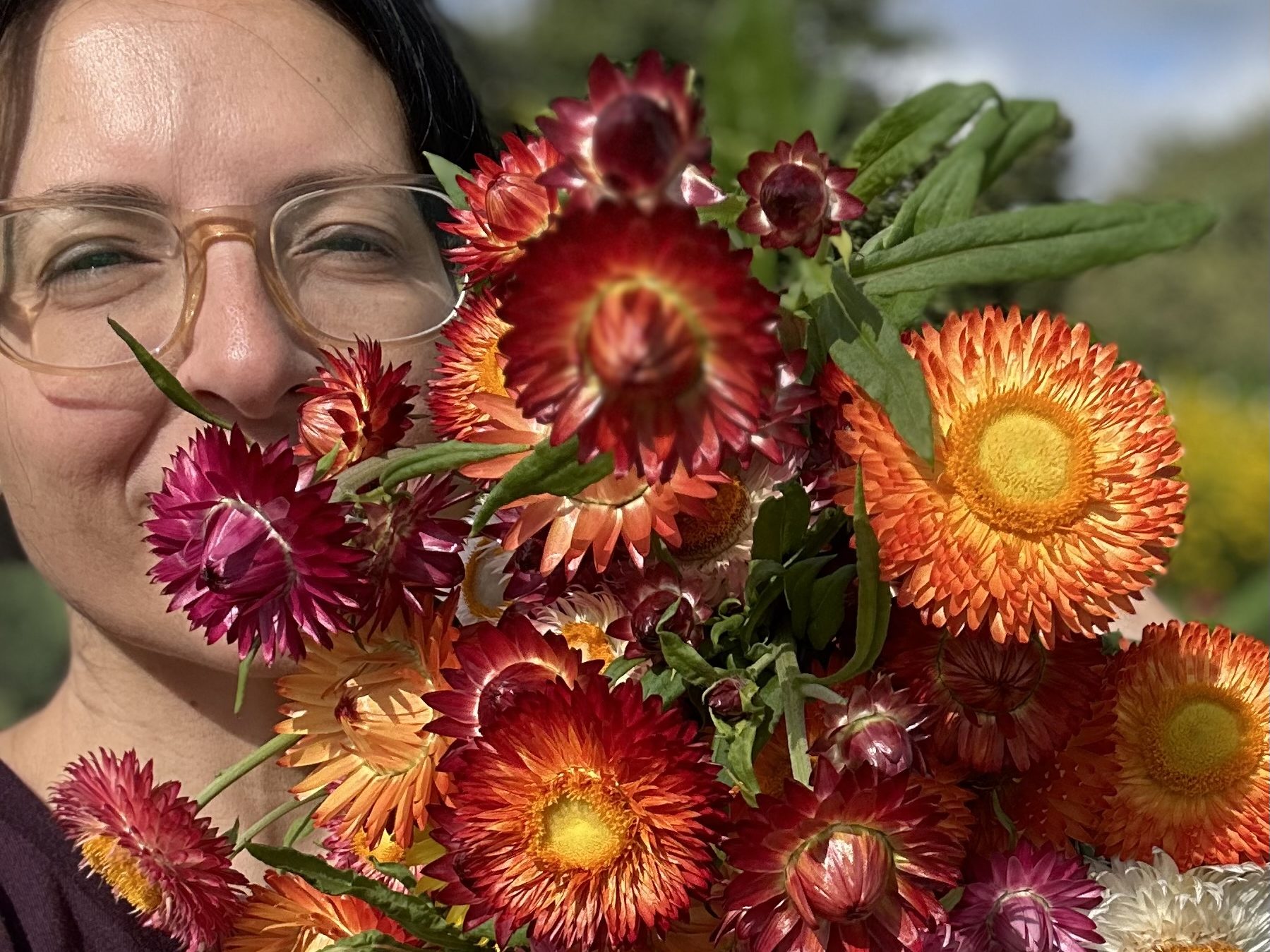Ellen Mary in the garden with a bunch of cut orange, red and pink dahlias