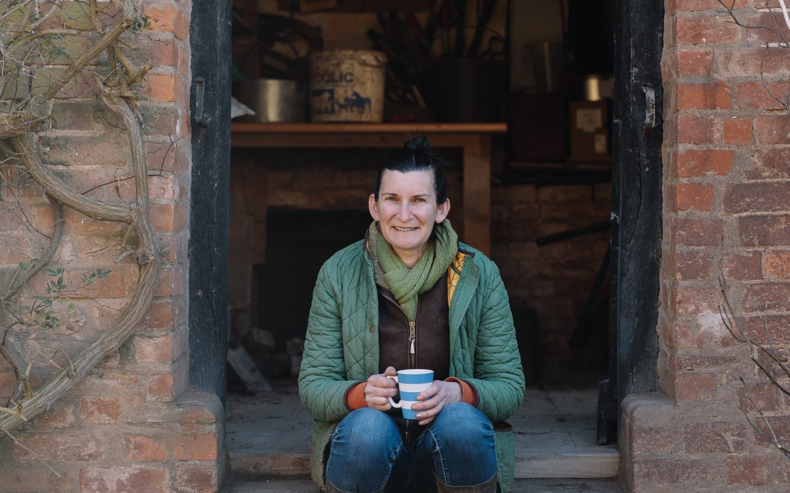 Tamsin Westhorpe sat at the entrance to a home holding a mug of tea