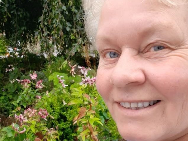 a close up of Katherine Crouch in the garden with pink flowers in the background