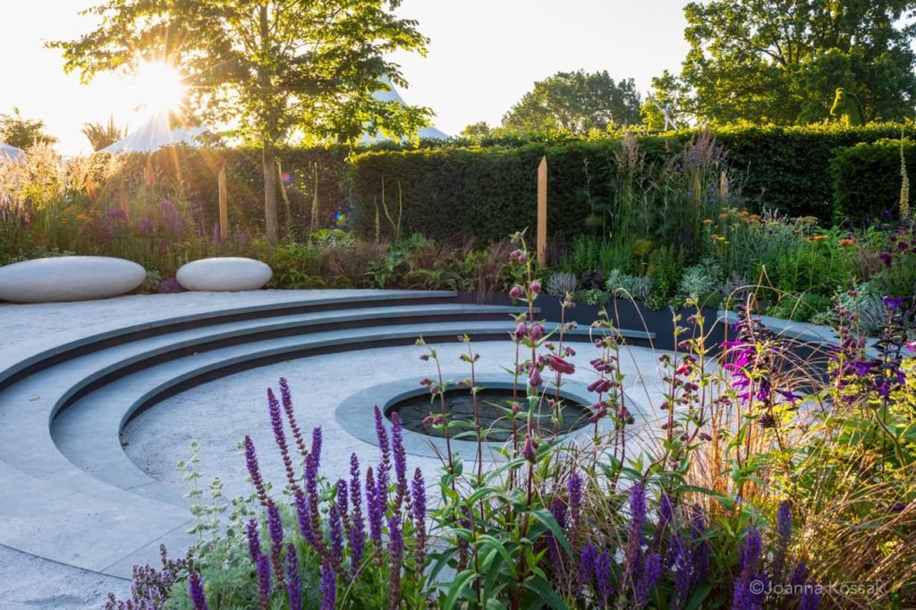 circular patio design on levels surrounded by brightly coloured flowering plants