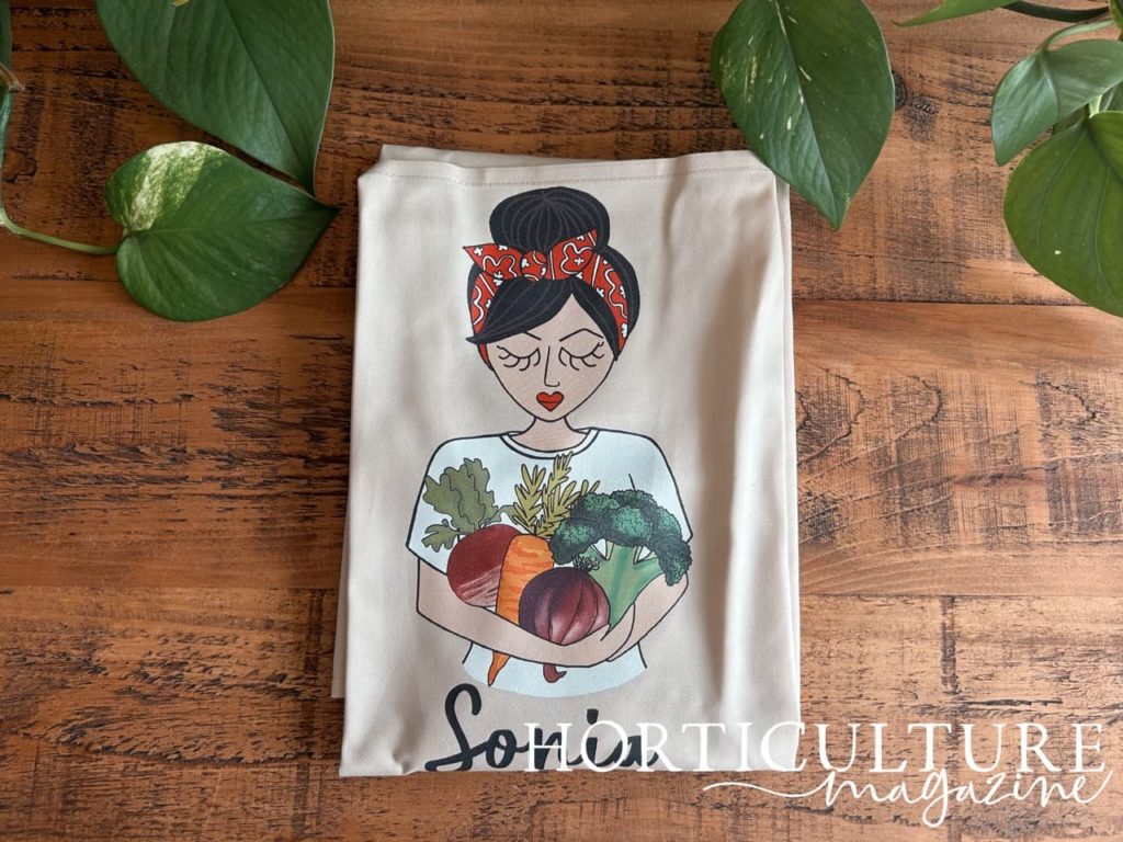 close-up of the illustrated print of a woman holding veggies on the front of a folded apron