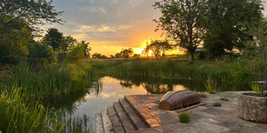 sun setting behind a landscape with a pond designed by Todd Longstaffe-Gowan