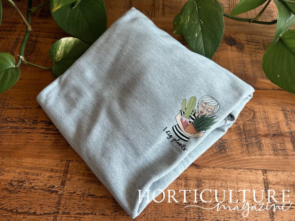 grey jumper with a lady holding plants printed onto it's breast