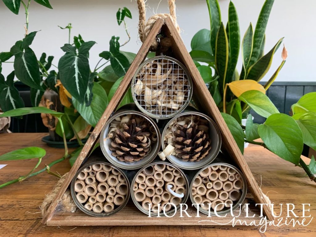 triangular bug hotel made from recycled tins filled with wood shavings, pinecones and bamboo canes