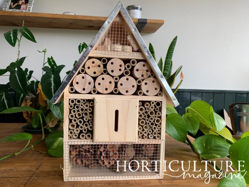 large insect hotel with shiny metal roof and several different compartments with pine cones in the bottom