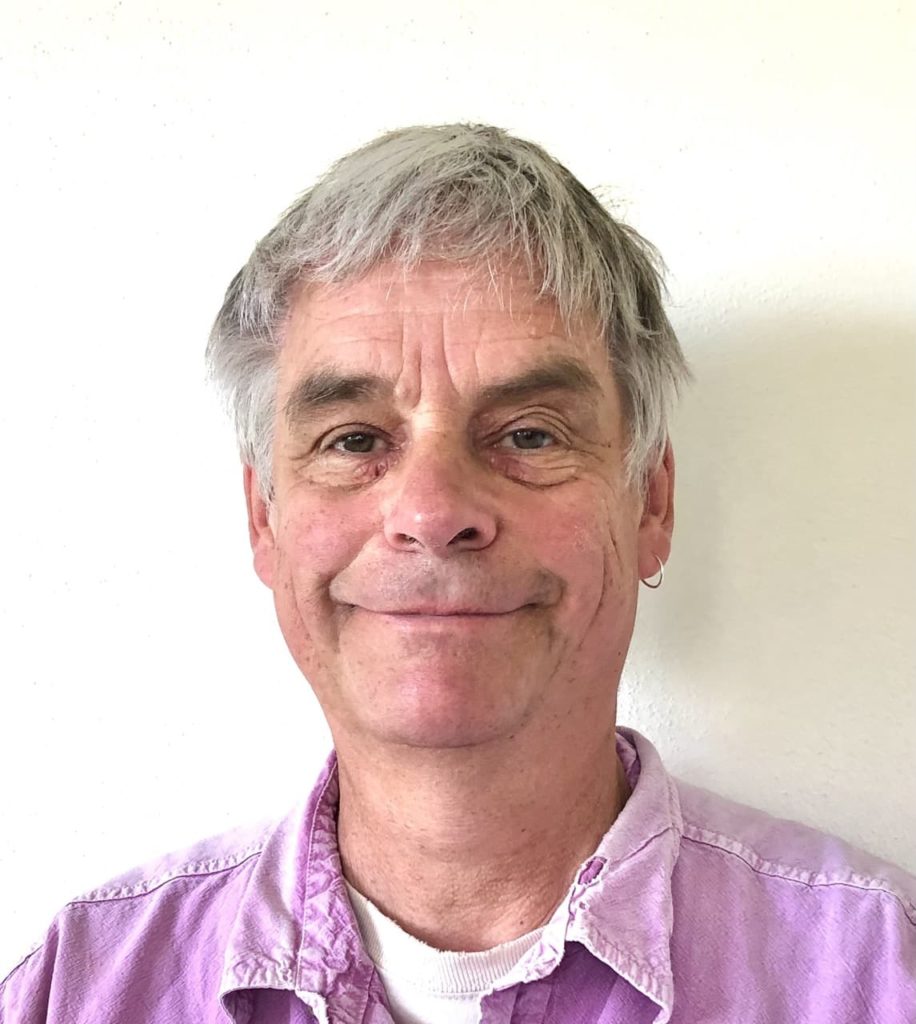 headshot of Noel indoors in front of a cream coloured wall