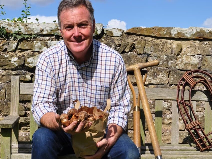 Martin Fish on a bench outside holding a handful of bulbs ready for planting